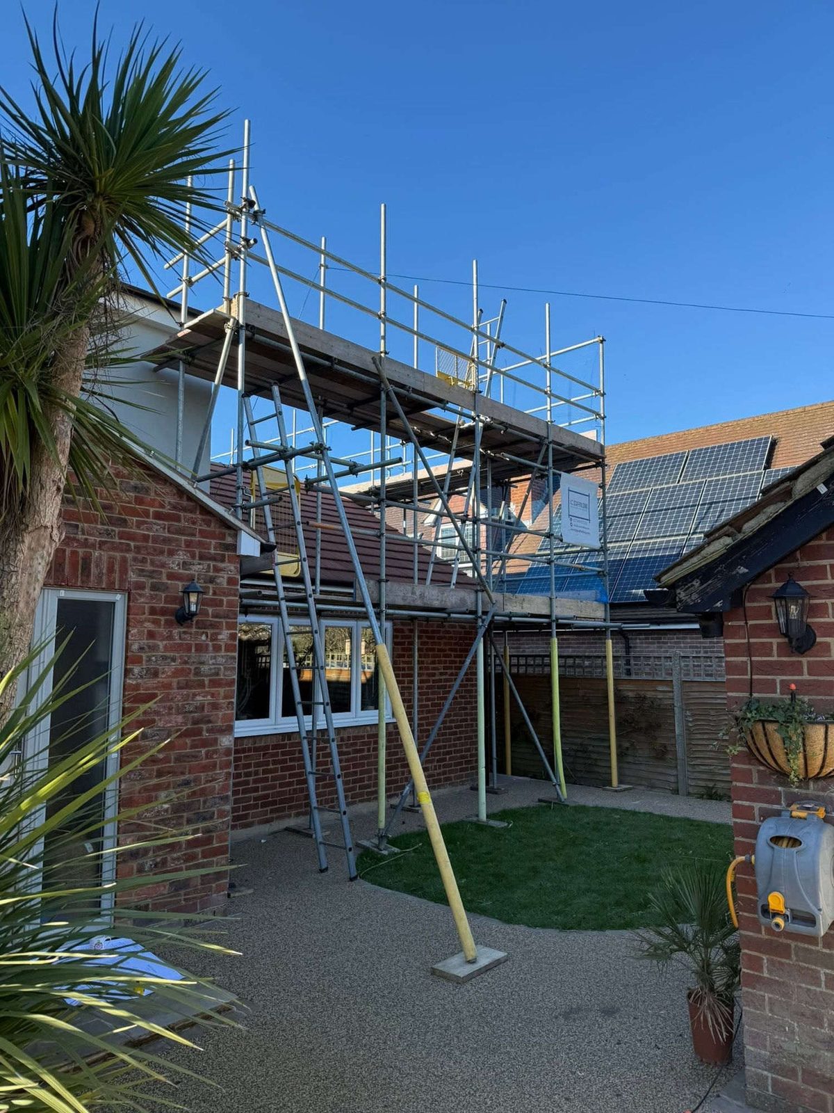 Boarded scaffold platform running alongside a solar array on a Kent roof, panels and roofline reachable from the same lift